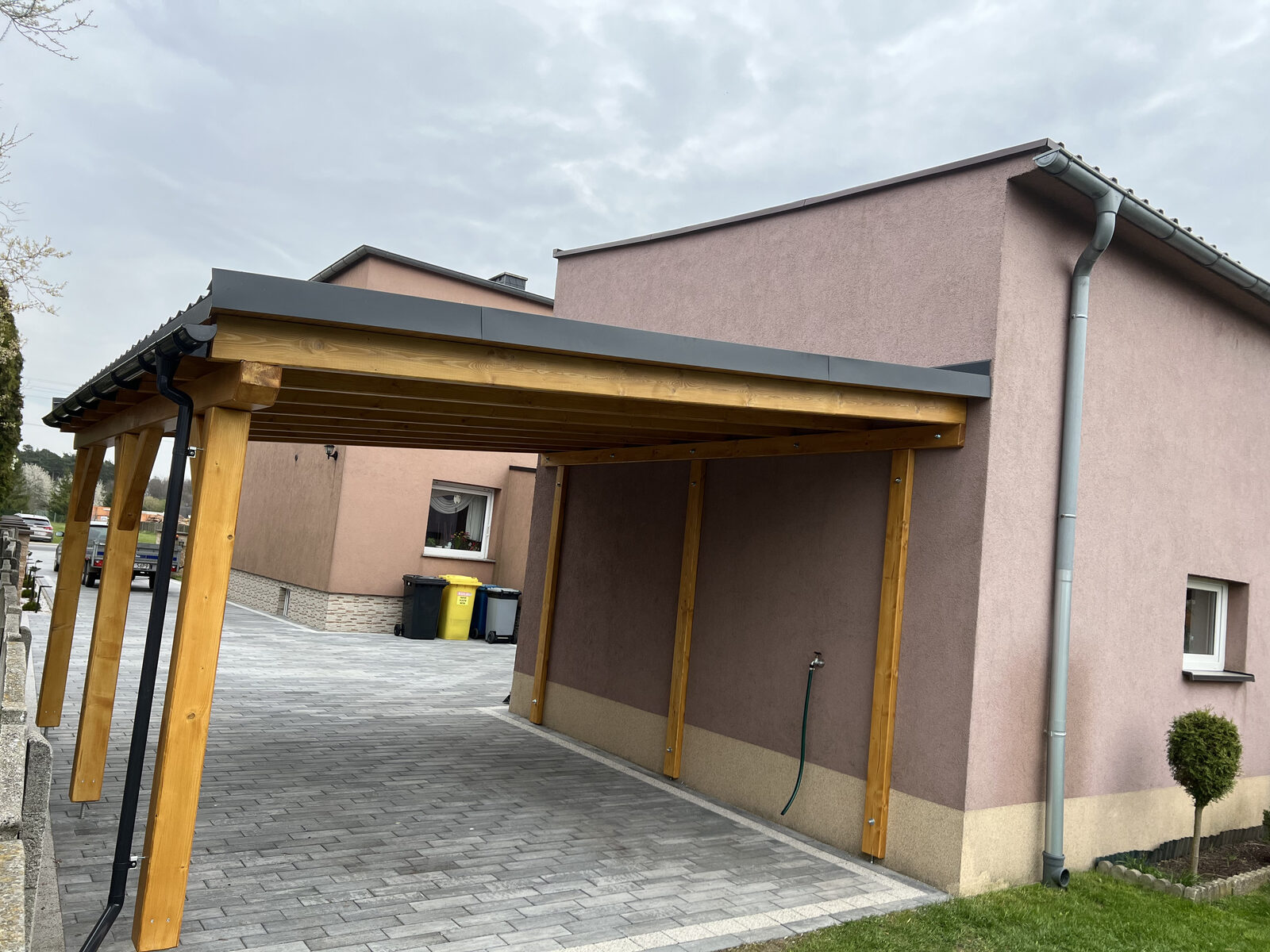 Wiata garażowa na konstrukcji drewnianej z dachem krytym blachą, dostawiona do budynku